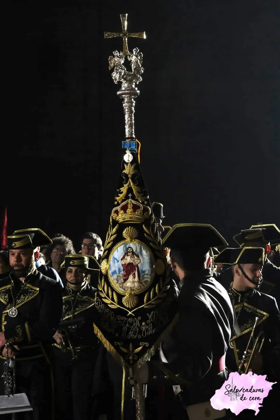 Primer plano del banderín de la agrupación: la imagen de San Salvador bordada en oro sobre terciopelo negro, bajo una corona real y rodeada de laurel.