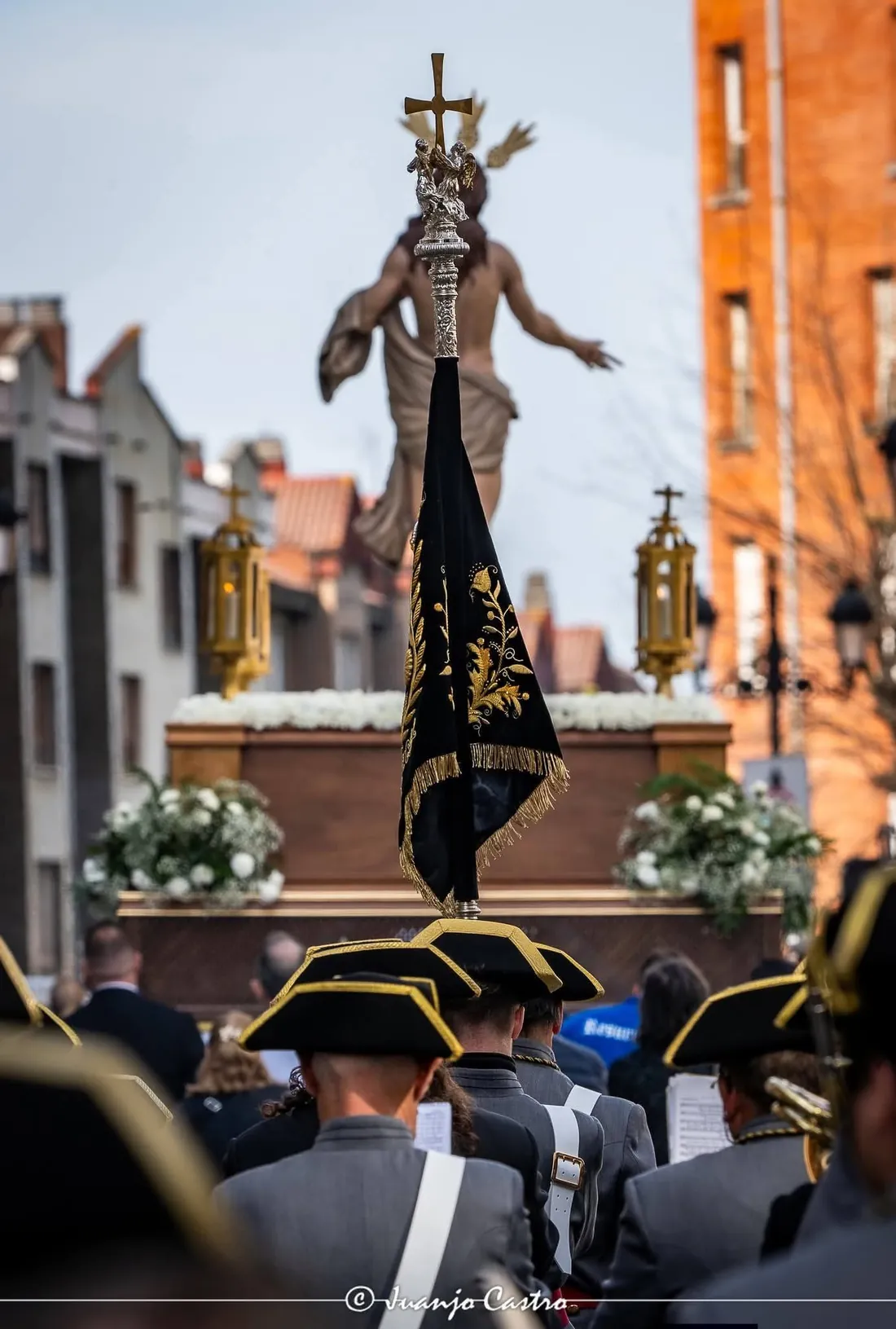 El banderín, con el mástil rematado por una cruz, delante del paso del Resucitado en una calle de Oviedo.