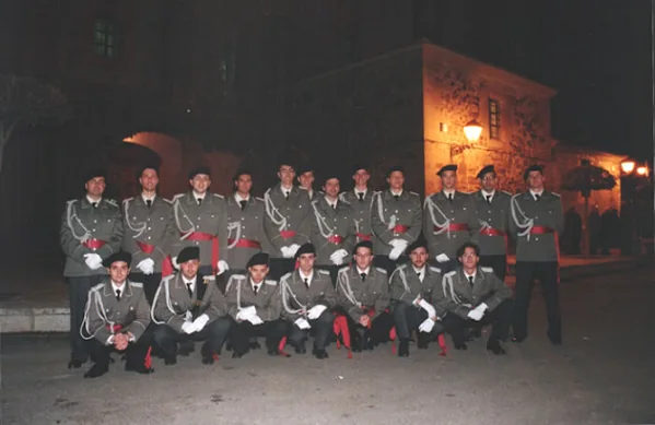 Foto de grupo de la agrupación de noche, unos sentados en el suelo y otros de pie, con el uniforme gris.